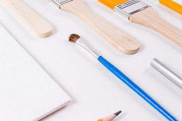 Education art concept. Set of different sizes brushes, blank canvas and various pencils on light background. Drawing supplies. Diagonal layout. Open composition.
