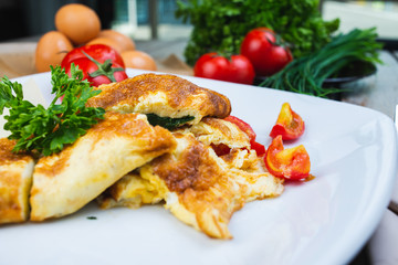 Traditional omelet with vegetables, spinach, tomatoes and herbs on a wooden table in a restaurant.