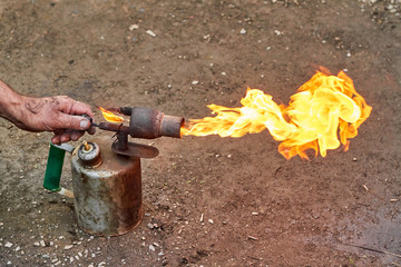 Male hand adjusts flame at the old rusty blowtorch.
