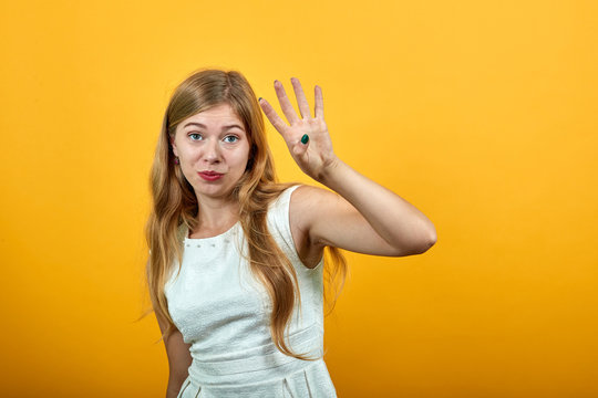 Charming blonde caucasian young woman showing four fingers, looking at camera over isolated orange background wearing white shirt. Lifestyle concept