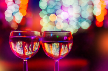 Holiday background. A pair of Glasses of wine, champagne on a background of bright multi-colored bokeh. Concept of a solemn feast, congratulations on Valentine's Day, Christmas