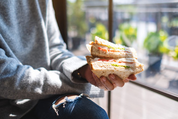 Closeup image of a woman holding and eating whole wheat sandwich in the morning