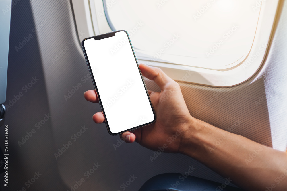 Wall mural mockup image of a hand holding a black mobile phone with blank desktop screen next to an airplane wi