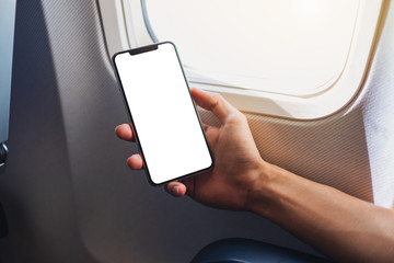 Mockup image of a hand holding a black mobile phone with blank desktop screen next to an airplane...