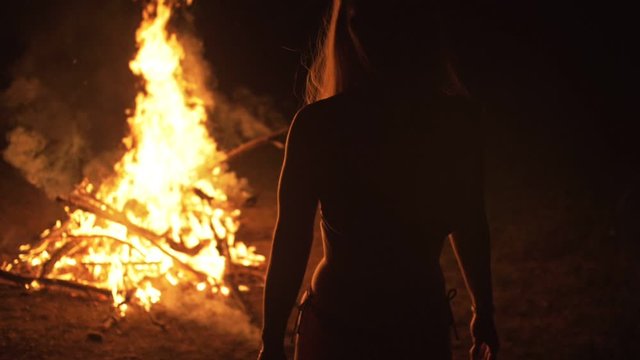 Silhouette of mystic woman in black background of fire fly flame, spark, of contour outline. Adult sexy of young girl witchcraft ceremony ritual dance in underclothes. Outdoor slow motion. Caucasian.
