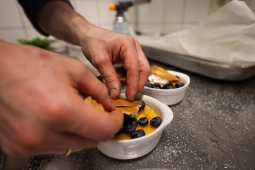 chef preparing creme brulee with bleberries in commercial kitchen