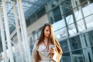 Fototapeta premium Business woman with the phone near office. Portrait of beautiful smiling female with phone, standing outdoors. Phone communication.