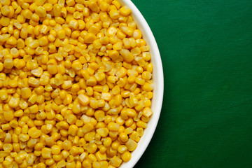 canned corn in white plate top view. green background	