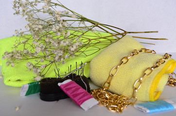 multi-colored threads, needles, a gold chain on a yellow fabric and white flowers on a white background
