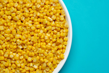 canned corn in white plate top view.  turquoise, light blue background