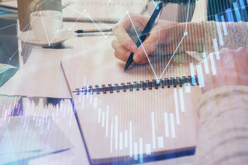 Forex chart hologram on hand taking notes background. Concept of analysis. Double exposure