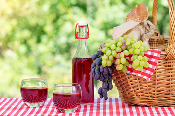 Picnic basket, grapes, juice and baguette on a red tablecloth