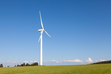Fototapeta premium Single wind turbine in a lush green hilltop pasture providing green renewable energy