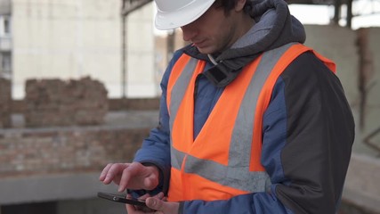 Builder in a white helmet with a smartphone at a construction site