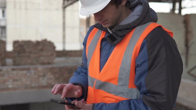 Builder in a white helmet with a smartphone at a construction site