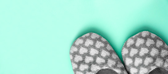 Pair of gray fluffy slippers with white hearts on neo mint background. Warm cozy home footwear. Sweet home, relaxation, coziness, hygge concept. Top view. Copy space