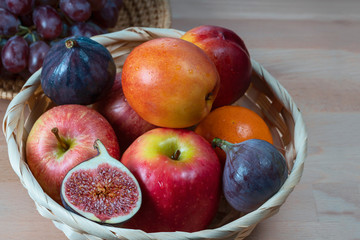  fresh fruits and red grape berries in a straw basket on a light wooden background