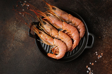 .Four langoustines on a black corrugated round plate on a dark background. Image with a horizontal orientation and copy space.