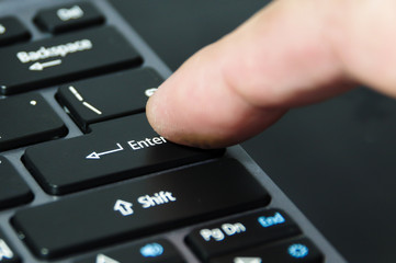 A finger hitting enter button on notebook keyboard.