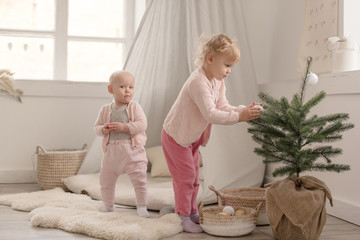 Two cute little baby girls play in a spacious bright minimalistic children's room.