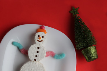 Edible snowman on a plate. Dessert. Red background. Christmas concept
