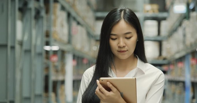 Beautiful business woman using tablet for choose product in a large industrial room of a furniture warehouse.