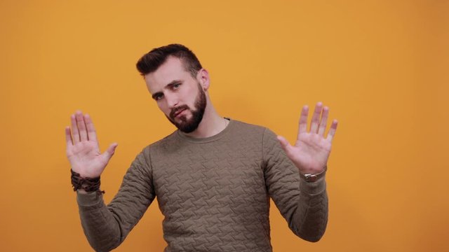 Charming handsome caucasian man over isolated orange background wearing fashion green sweater showing palms at camera, keeping mouth opened