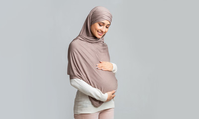 Pregnant muslim girl in hijab tenderly touching her belly