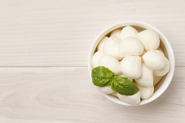 Mozzarella cheese in a bowl with basil on a wooden white table. Place for text.