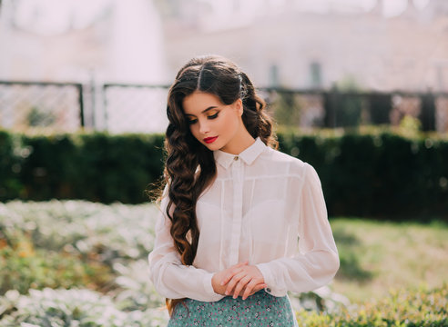 portrait brunette girl. long hair hairstyle curls waves Hollywood retro style. Gentle makeup red lips black liner eyeliner. White vintage blouse. urban sunny day. Glamorous outfit stylish schoolgirl