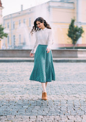 woman brunette student is walking around street city outdoors. Long wavy hair flying in motion. cheerful happy girl. face smile. white vintage blouse, mint midi skirt brown retro boots. floral print