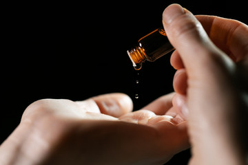 skin care and treatment - woman pouring oil in a hand from vial on black background - obrazy, fototapety, plakaty
