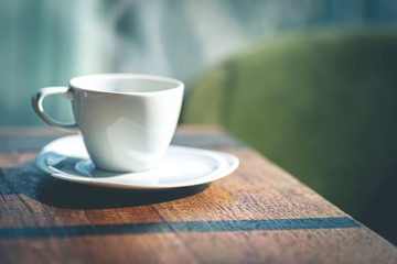 A white ceramic coffee cup with saucer on the wooden table indoors.