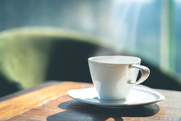 A white ceramic coffee cup with saucer on the wooden table indoors.