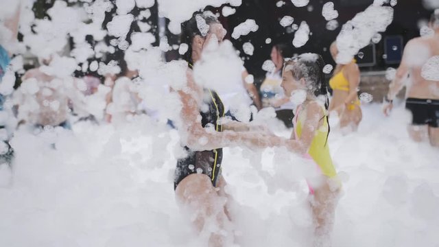 Mom and her little daughter play with soap and foam in a crowd of tourists at a beach party in a resort hotel