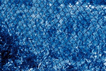 Wire fence or metal net on blurred background toned in color of the year 2020 classic blue