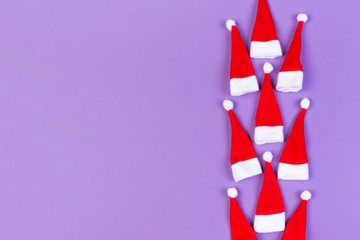 Fototapeta premium Top view od stylish red Santa hats on colorful background. Merry Christmas concept with copy space