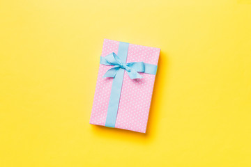 Gift box with blue bow for Christmas or New Year day on yellow background, top view with copy space