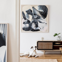 Design scandi home interior of living room with wooden commode, black rattan pouf, plant and elegant accessories. Stylish home decor. Mock up abstract paintings. Dog is lying on the floor. Template.
