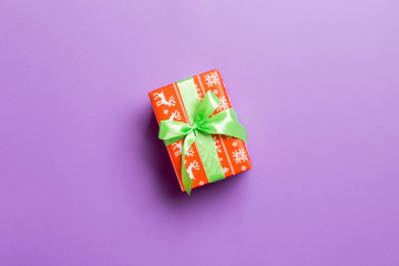 Gift box with green bow in hands for Christmas or New Year day on purple background, top view with copy space