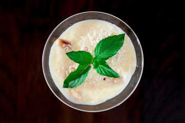 Two glasses of sweet milk dessert with coconut, peanuts and mint on black background with copy space