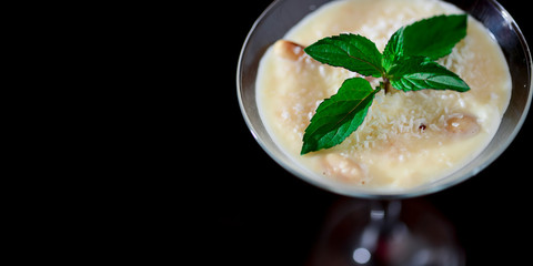 Two glasses of sweet milk dessert with coconut, peanuts and mint on black background with copy space