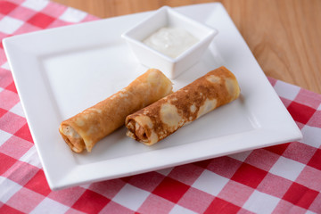 Frech crepes, two savoury pancakes made with flour and milk served with sour cream on a plaid background.