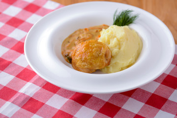 Traditional cuisine, mashed potatoes with gravy, meat and dill served on a white plate on a plaid background