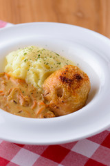 Traditional cuisine, mashed potatoes with gravy, meat and dill served on a white plate on a plaid background