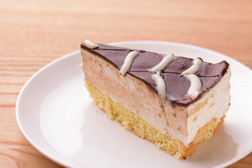 Sweet chocolate spider web cake with frosting on top served on a white plate on light wooden background.