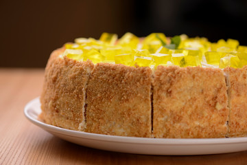 Lemon multi layered cake decorated with citron jelly and mint served on white plate on wooden background.
