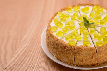 Lemon multi layered cake decorated with citron jelly and mint served on white plate on wooden background.