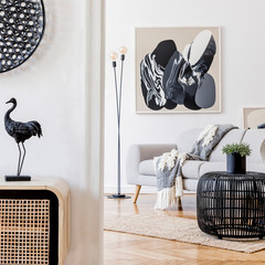 Scandinavian and design home interior of open space with wooden commode, gray sofa, design black rattan decoration, tropical leafs and elegant personal accessories. Stylish art home decor. Template.