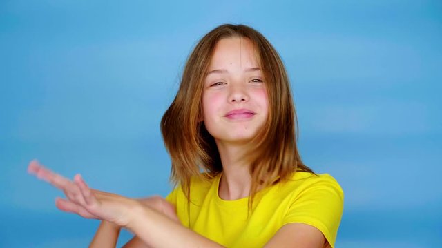 Happy teen girl in a yellow t-shirt is dancing, smiling and fools around. Blue background with copy space. Teenager emotions. 4k footage